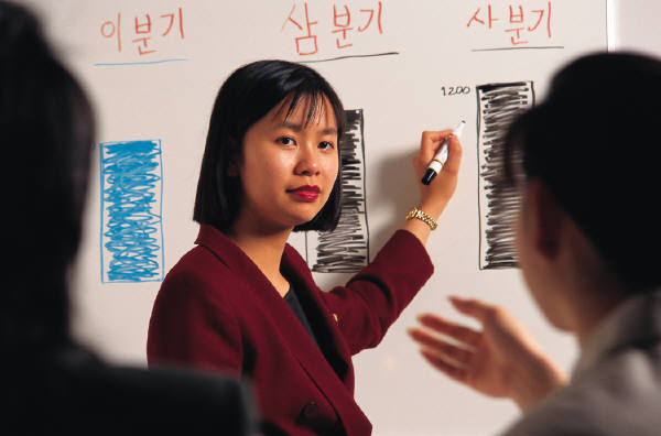 A woman of oriental background pointing to white board markings while instructing a group